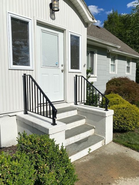 Front entrance of a white house with small concrete steps, black railings, and a front door surrounded by windows.
