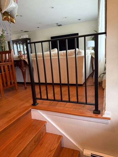 Black stair railing beside carpeted living room with hardwood steps and beige sofa in the background