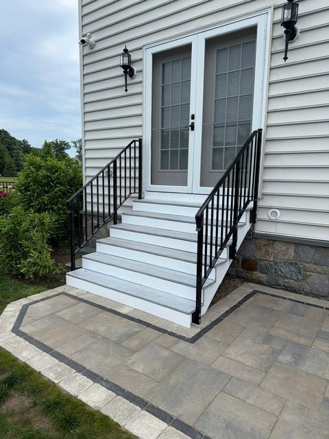 Front steps with black railings leading to white double doors on a house exterior.