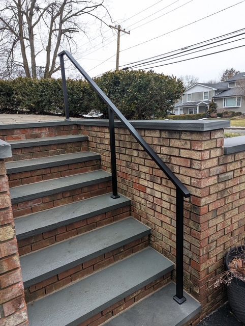 Outdoor brick stairway with black metal handrail and gray steps beside a brick wall