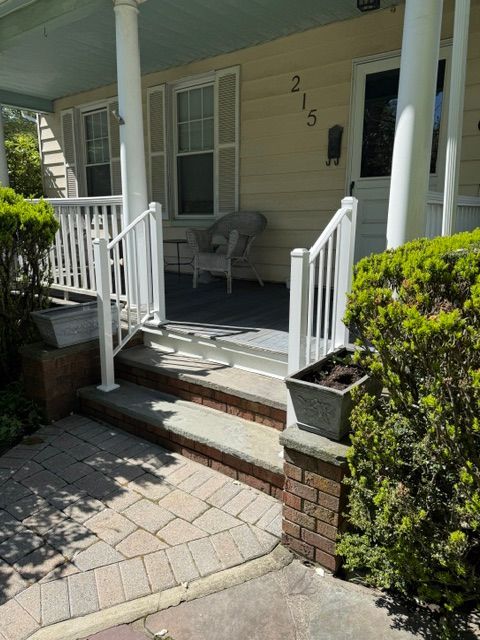 Front porch with two steps, white railings, and a chair outside house number 215.