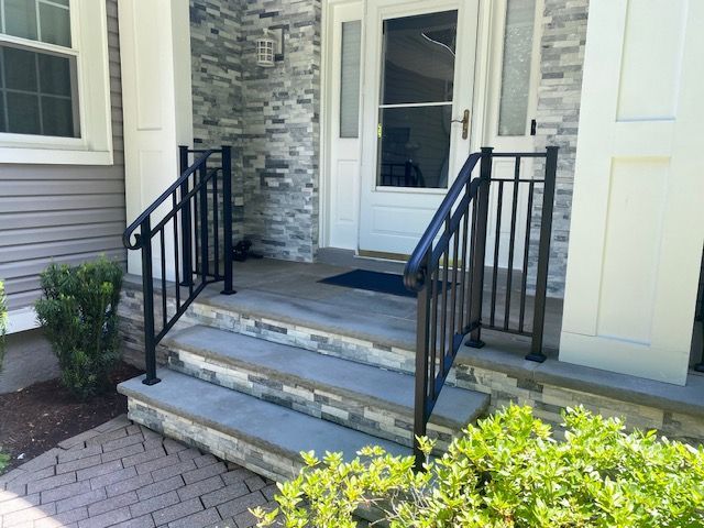 Front steps with black railings leading to a white front door and stone facade
