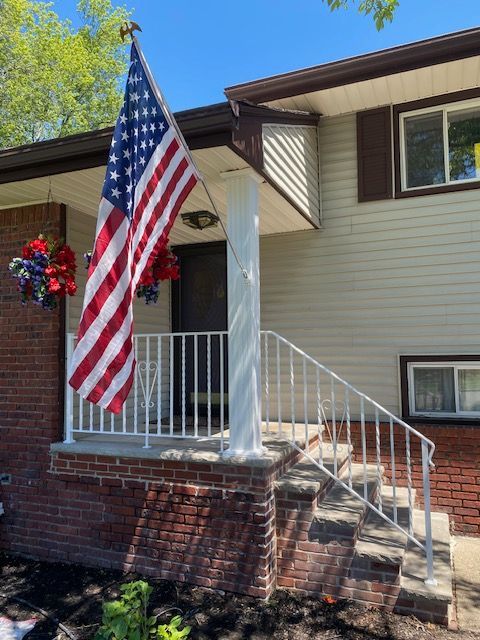 Front porch with American flag, white columns, brick steps, and beige house exterior