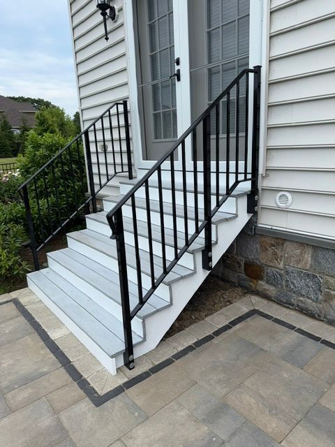 White front steps with black railings leading to a house entrance beside a stone wall.