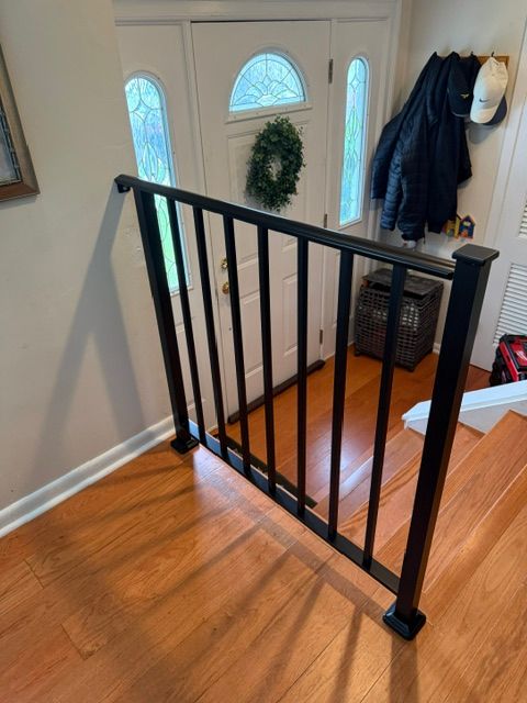 Black stair gate blocking a staircase beside a front door and coat hooks