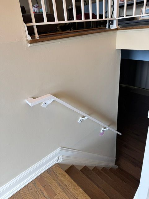 White stair handrail on beige wall beside wooden steps and a railing opening
