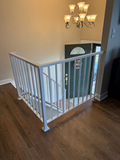 Upstairs hallway landing with white railing, hardwood floor, and chandelier above stairwell opening