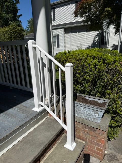 White metal handrail beside a porch ramp next to a brick wall and green shrubbery