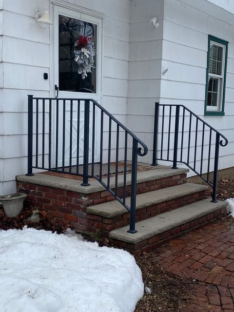 Front steps of a white house with black railings, brick risers, and snow on the left side.