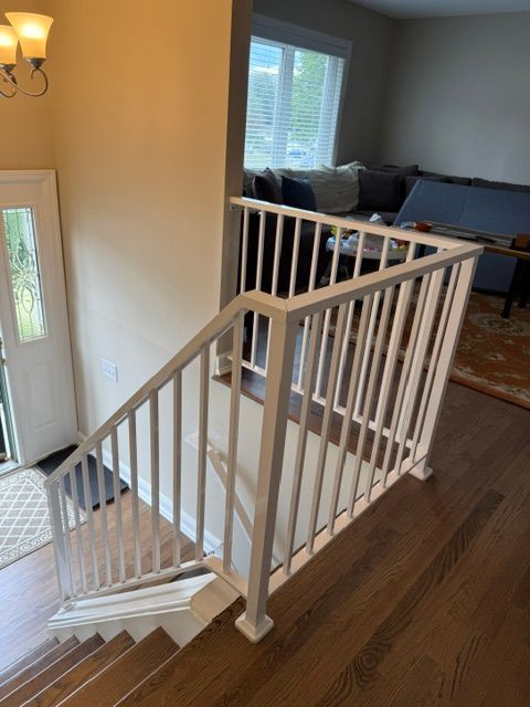 Stair landing with white railing, hardwood floors, and a view into a living room and front door.