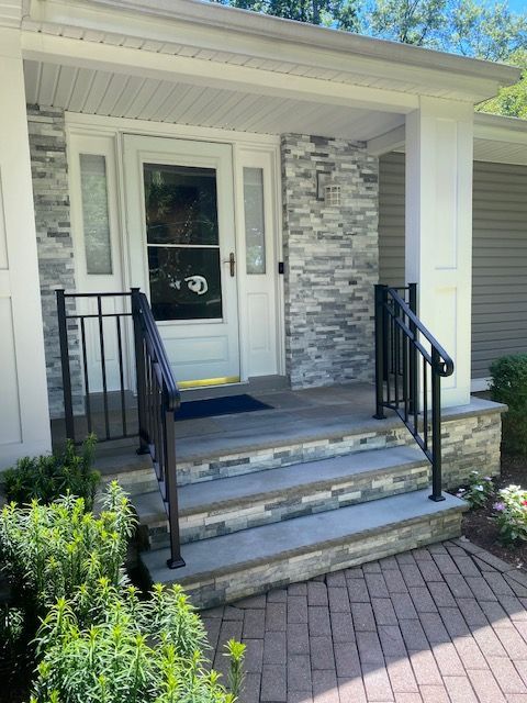 Front porch with white door, black railings, and three concrete steps beside a brick walkway