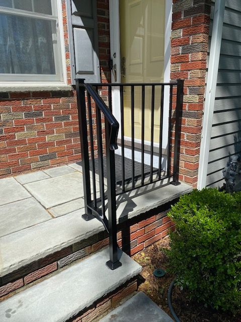 Brick house porch with a black metal handrail and concrete steps leading to the entrance