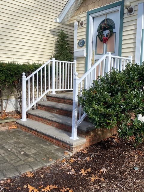 Front porch with white railings, brown steps, and a wreath on the door at a house entrance.
