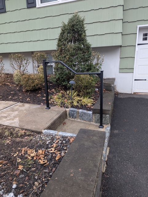 Accessible front path with concrete steps, black handrails, and a small landscaped bed beside a house