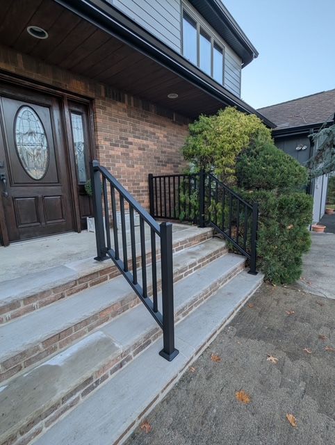 Front steps of a brick house with black railings and a dark wooden front door