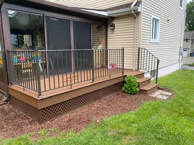 Raised back deck with black railing, brown lattice skirting, and steps down to a grassy yard