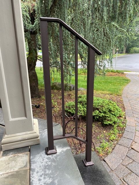 Black metal handrail beside concrete steps and a stone walkway in a landscaped garden.