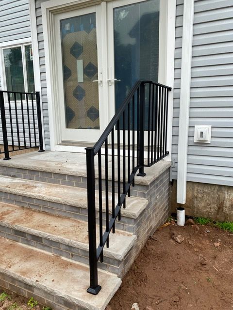 Front porch steps with a black metal handrail leading to a white door and vinyl siding