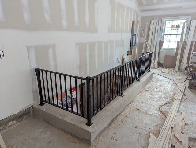 Indoor stairwell under renovation with black metal railing and unfinished walls