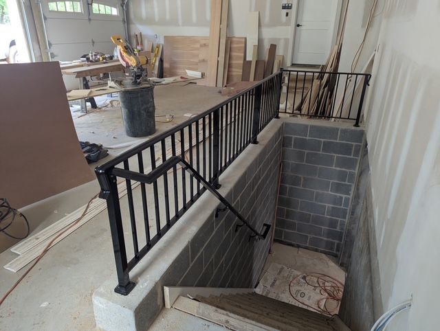 Basement stair opening with black metal railing and concrete block walls in a garage under construction