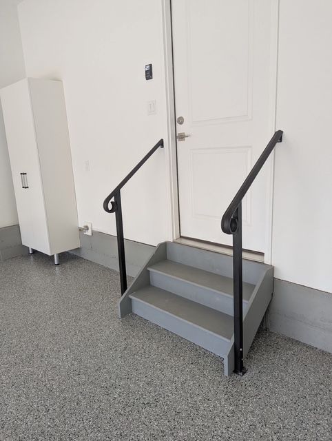 Small gray steps with black handrails leading to a white door in an indoor hallway