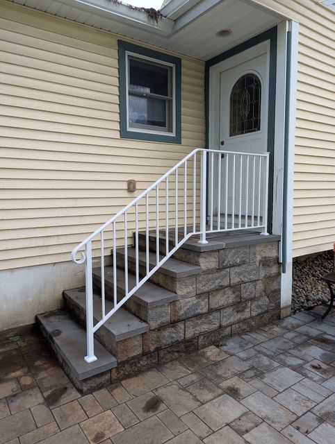 Exterior stone steps with a white metal railing leading to a side entrance door on a beige house.