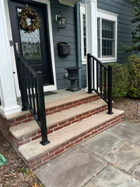 Brick front steps with black railings leading to a gray house entrance