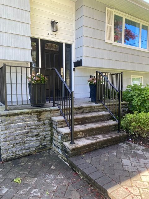 Front entrance with stone steps, black railings, and a white-sided house facade with a window.