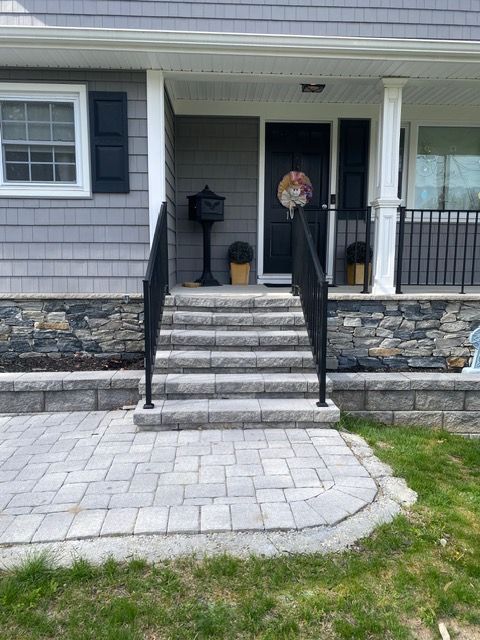 Front porch with stone steps, black handrails, and a curved paver walkway leading to the entrance