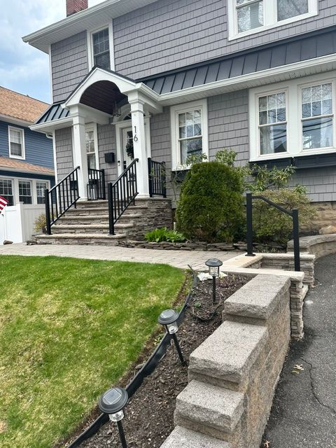 Front steps and porch of a gray house with black railings and a sloped front lawn