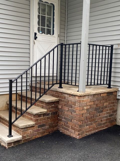 Front entrance with brick steps, black railing, and a white door beside a porch column.