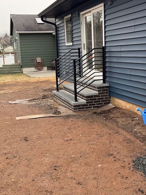 Exterior view of a house with steps and black metal railings leading to a sliding door. The steps are brick.