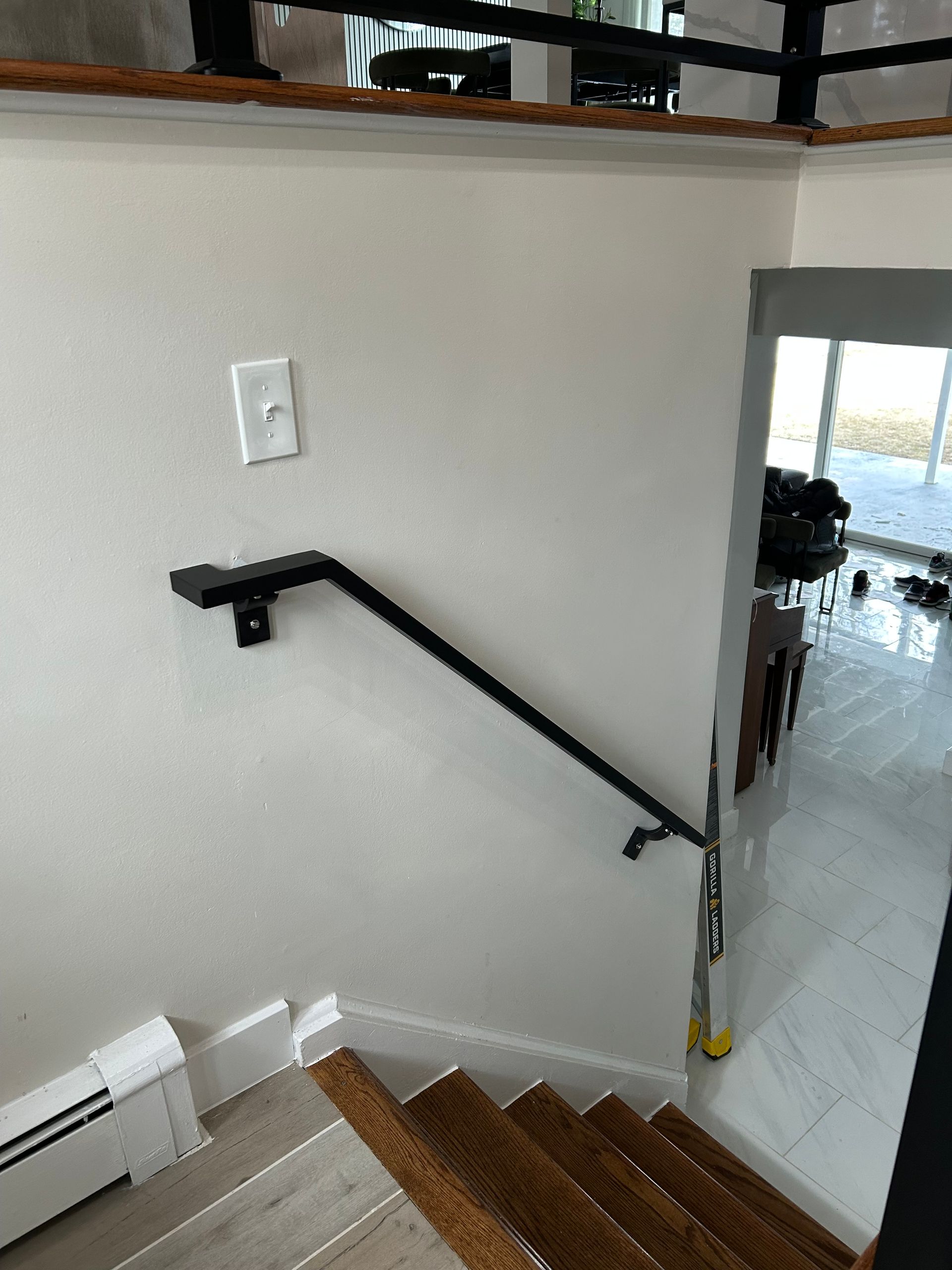 Black handrail mounted on white wall next to wooden staircase.