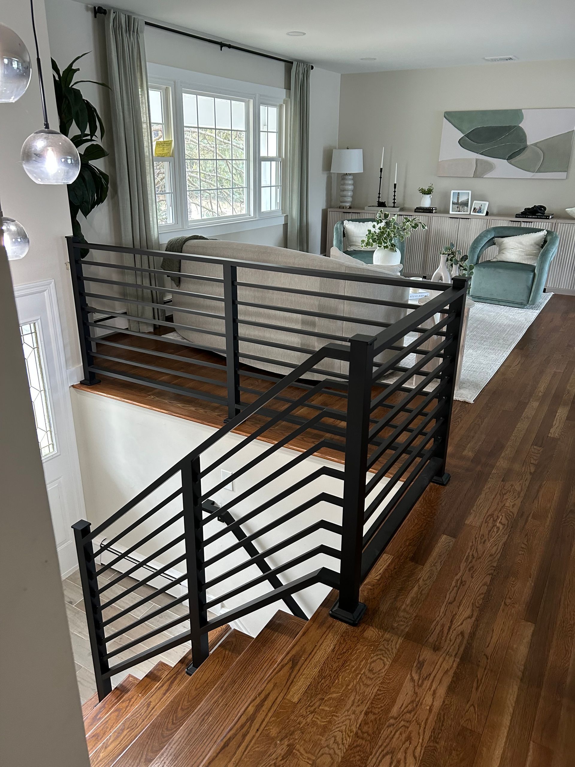 Interior view of a modern living area with a staircase and metal railing. Wooden floors and neutral color scheme.