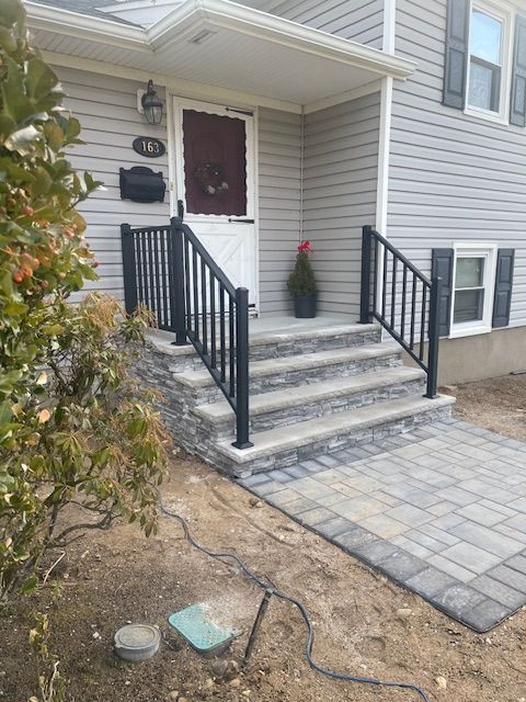 Exterior view of a house with stone steps, black railings, and a paver walkway leading to the front door.