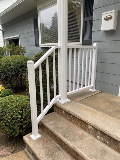 White railing on concrete steps leading to a house entrance. Bushes are on the side.