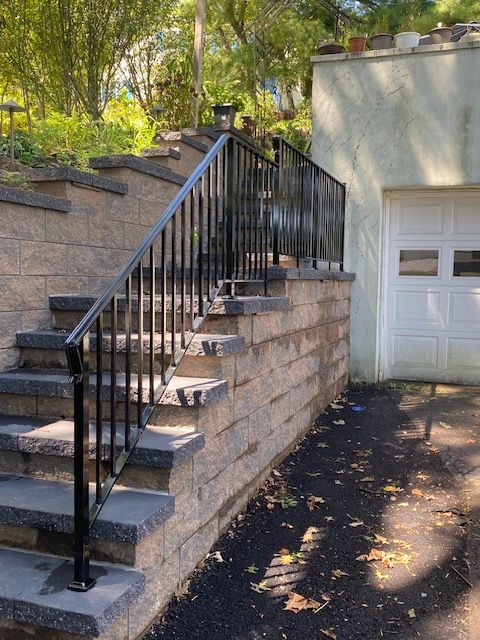 Exterior stairway with black metal railing and retaining wall leading to a garage.