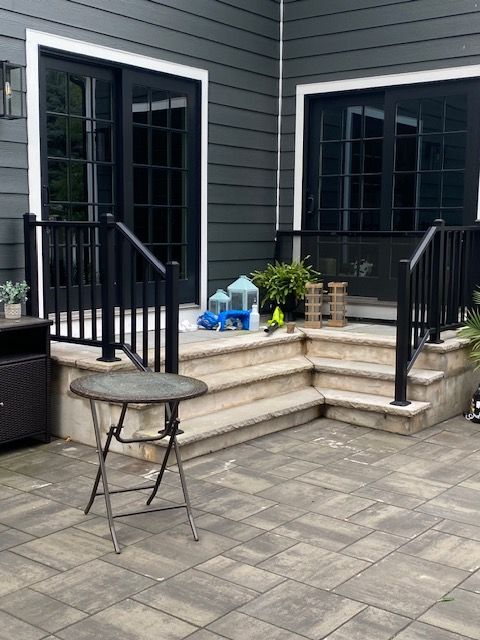 Dark gray house with black doors, steps, and railing.  A small table sits on brick patio.