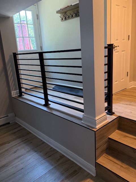 Black horizontal railing on a gray and wood-toned wall, leading to stairs. White door and trim.