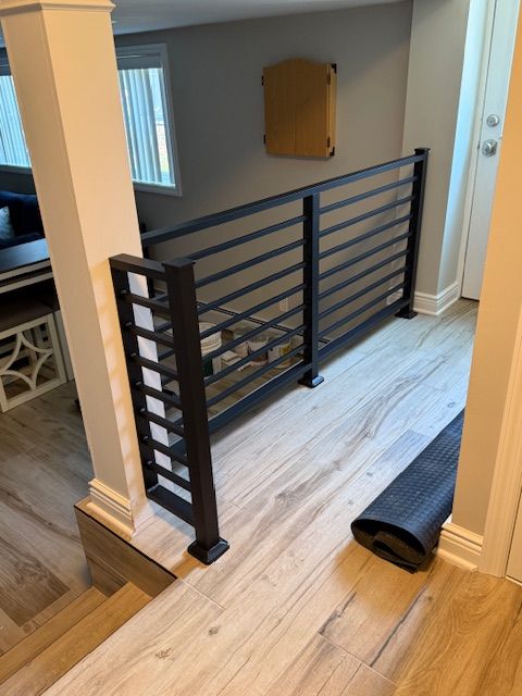 Black metal horizontal railing on light wood floor, leading to a doorway.