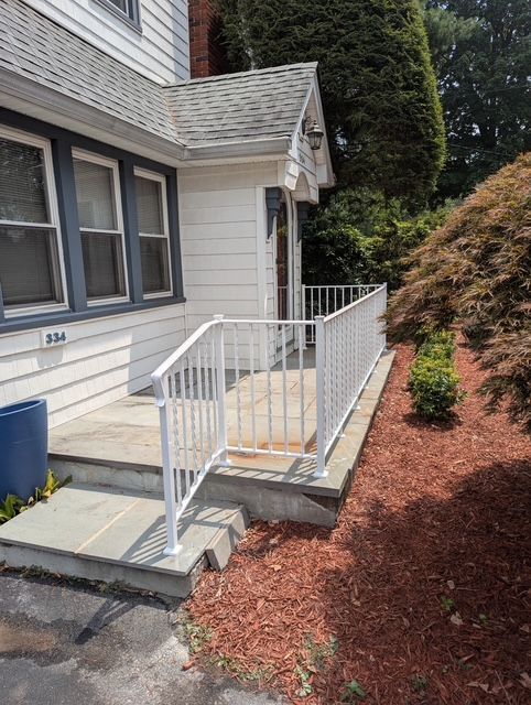 White railing and steps leading to a house entrance with blue siding and mulch.