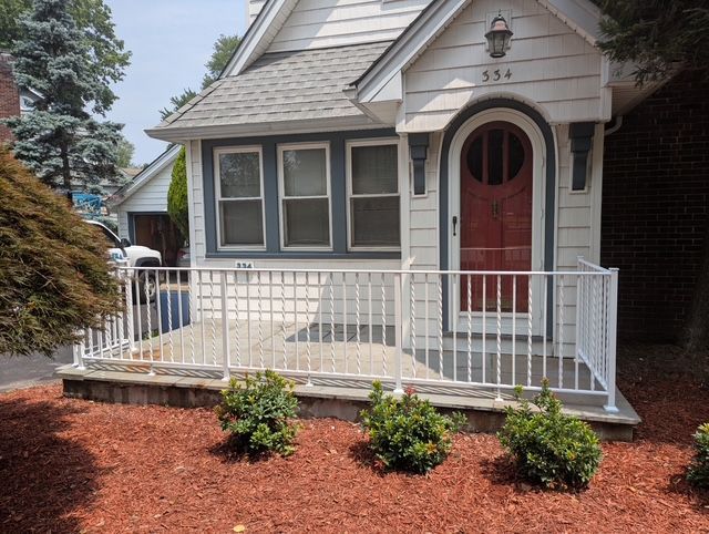 White house with a red door, small porch with white railing, bushes in front.