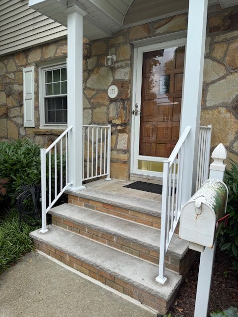 A front porch with white railings, steps, and a mailbox. A wooden door and stone exterior are visible.