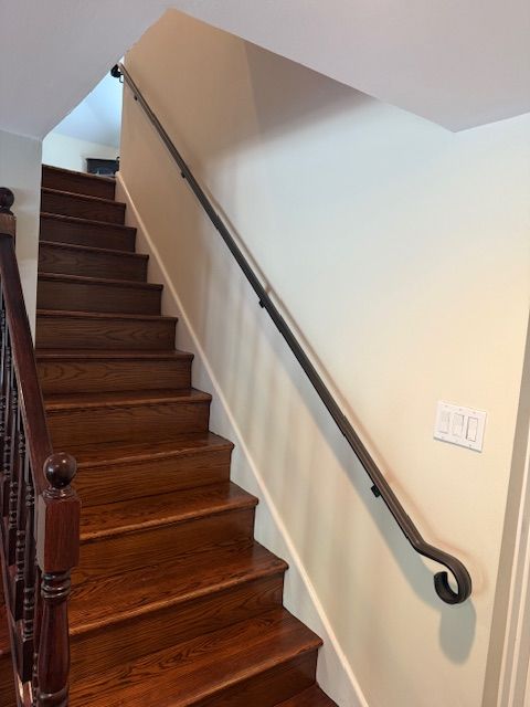 Wooden staircase with dark handrail and a simple black metal handrail on the wall. Beige walls.