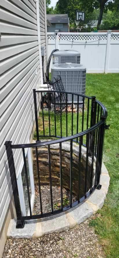Black metal railing around a basement window well on a house exterior.