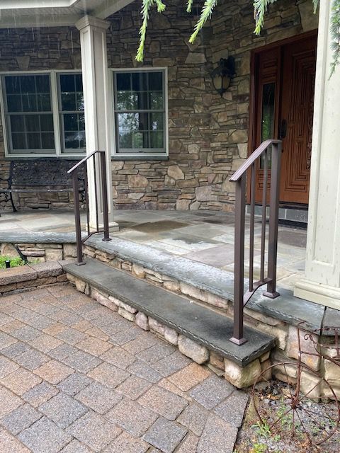 Brown handrails on a stone porch with steps leading to a front door.