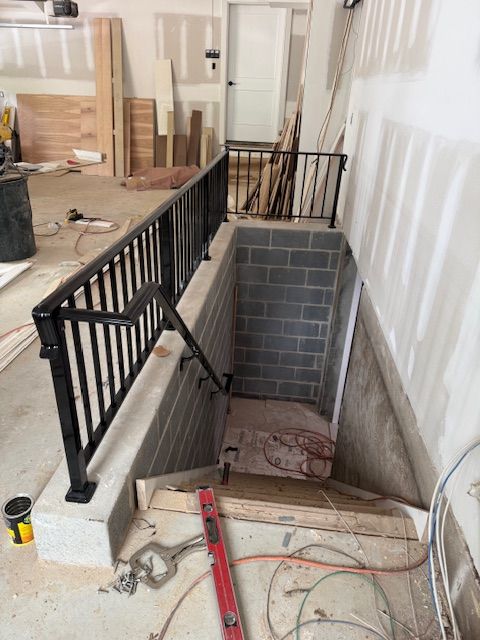 Black metal railing at stairwell entrance in a partially constructed basement. Concrete block walls and unfinished drywall.