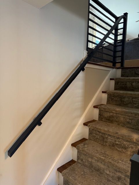 Black handrail along a staircase with gray carpeted steps and a matching black metal railing above.