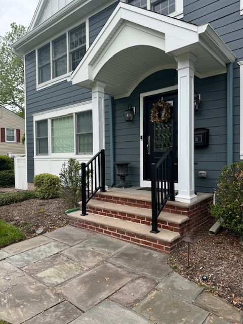 Front of a house with a porch. Gray siding, black door, brick steps, and stone walkway.