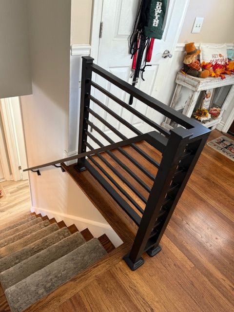 Black metal staircase railing with horizontal bars on wood floor stairs.